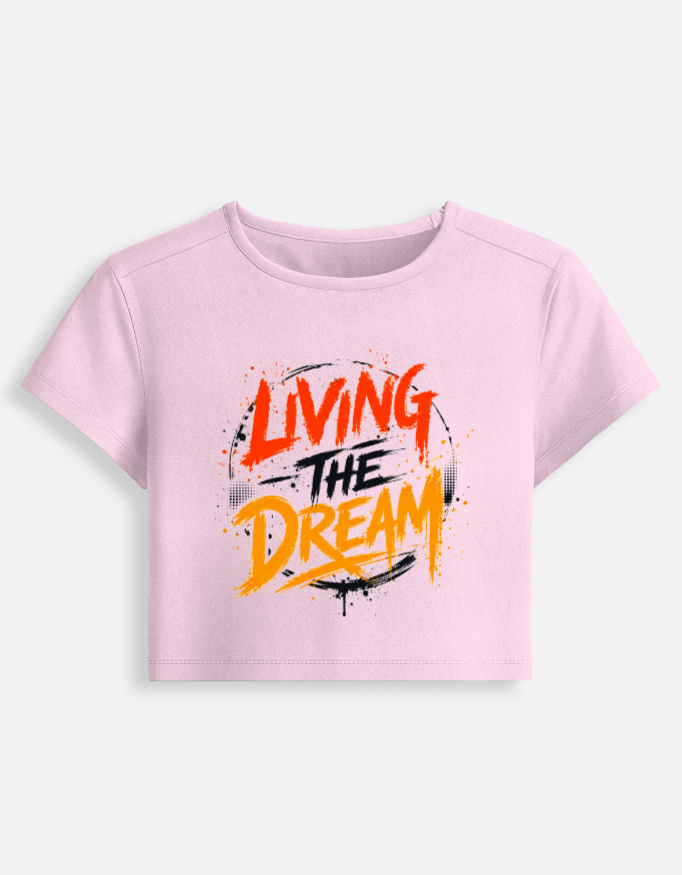 Light baby pink fitted baby tee featuring an energetic red, orange, and black graffiti spray typography graphic on the front that reads "Living The Dream".