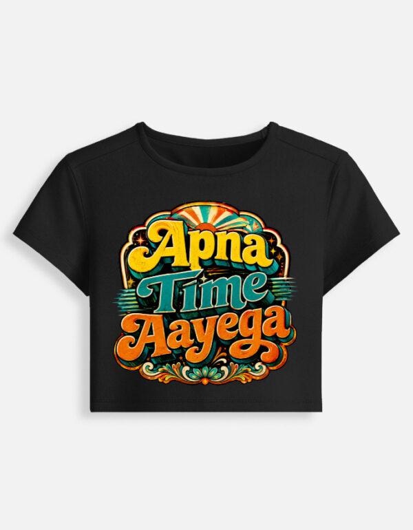 Black fitted baby tee featuring a vibrant retro psychedelic typography print on the front with the phrase "Apna Time Aayega" in bold yellow, teal, and orange letters.