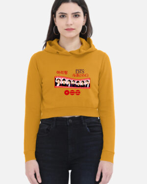 Woman wearing a mustard yellow cropped hoodie featuring a BTS "Arirang" film strip graphic print on the front with member portraits and Korean Hangul text.