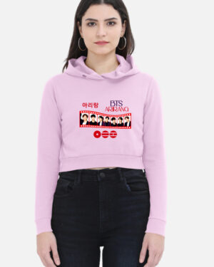 Woman wearing a light baby pink cropped hoodie featuring a BTS "Arirang" film strip graphic print on the front with member portraits and Korean Hangul text.